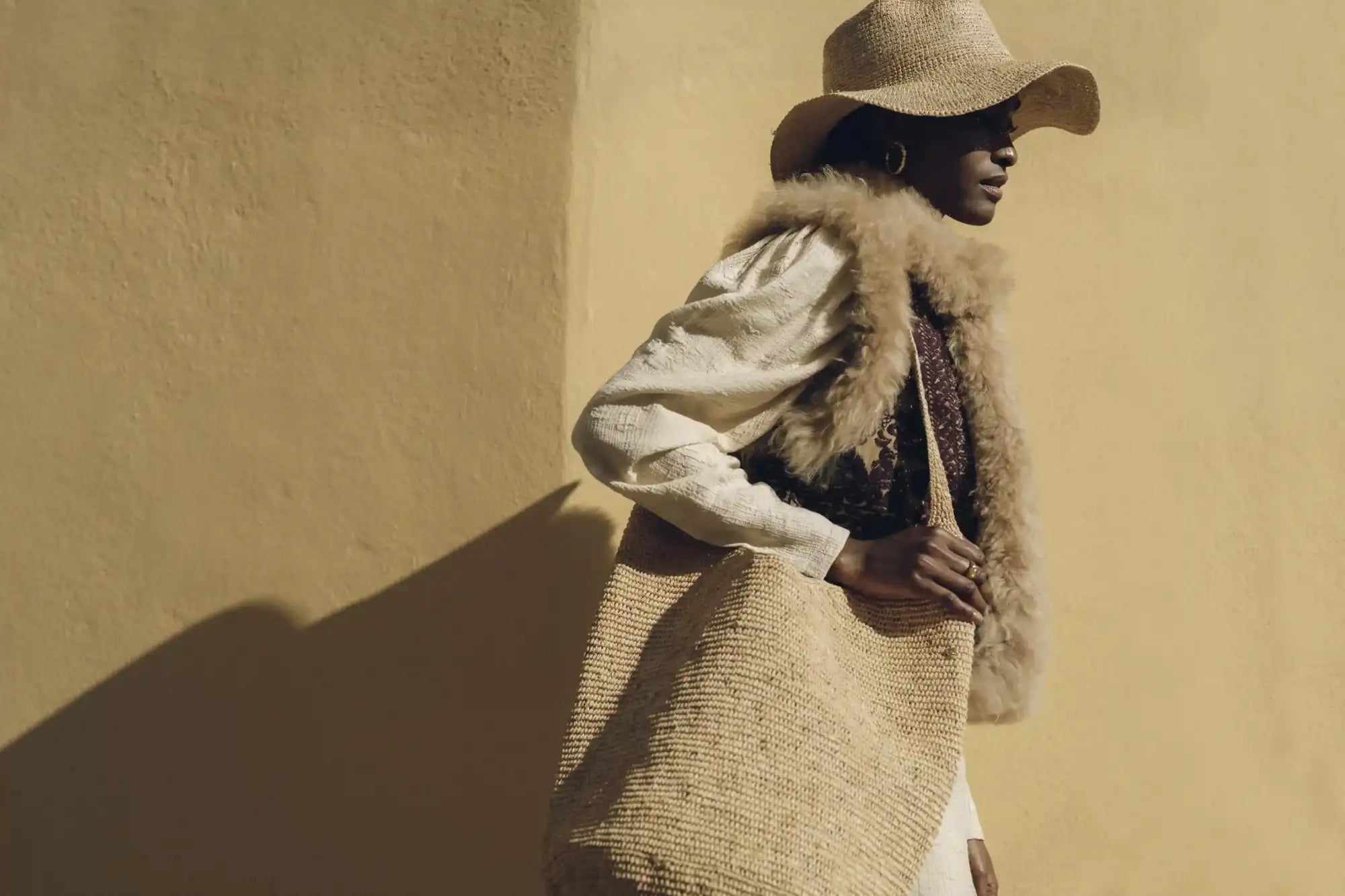 Beige woven straw tote bag with a textured, natural fiber weave and soft, light-colored fur trim along the top edge.