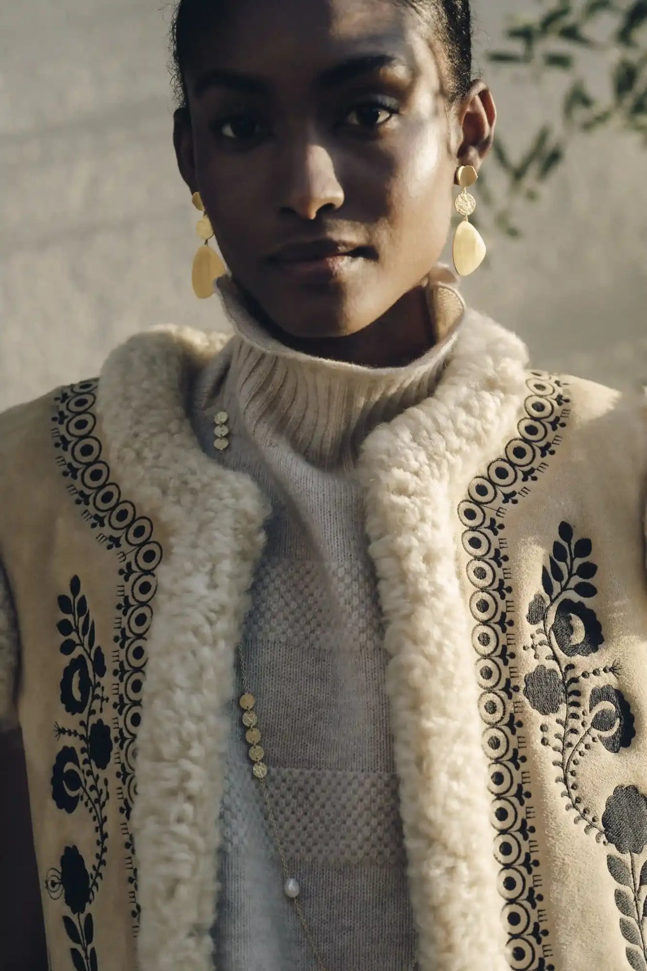 Cream-colored shearling vest with black embroidered floral and circular patterns.