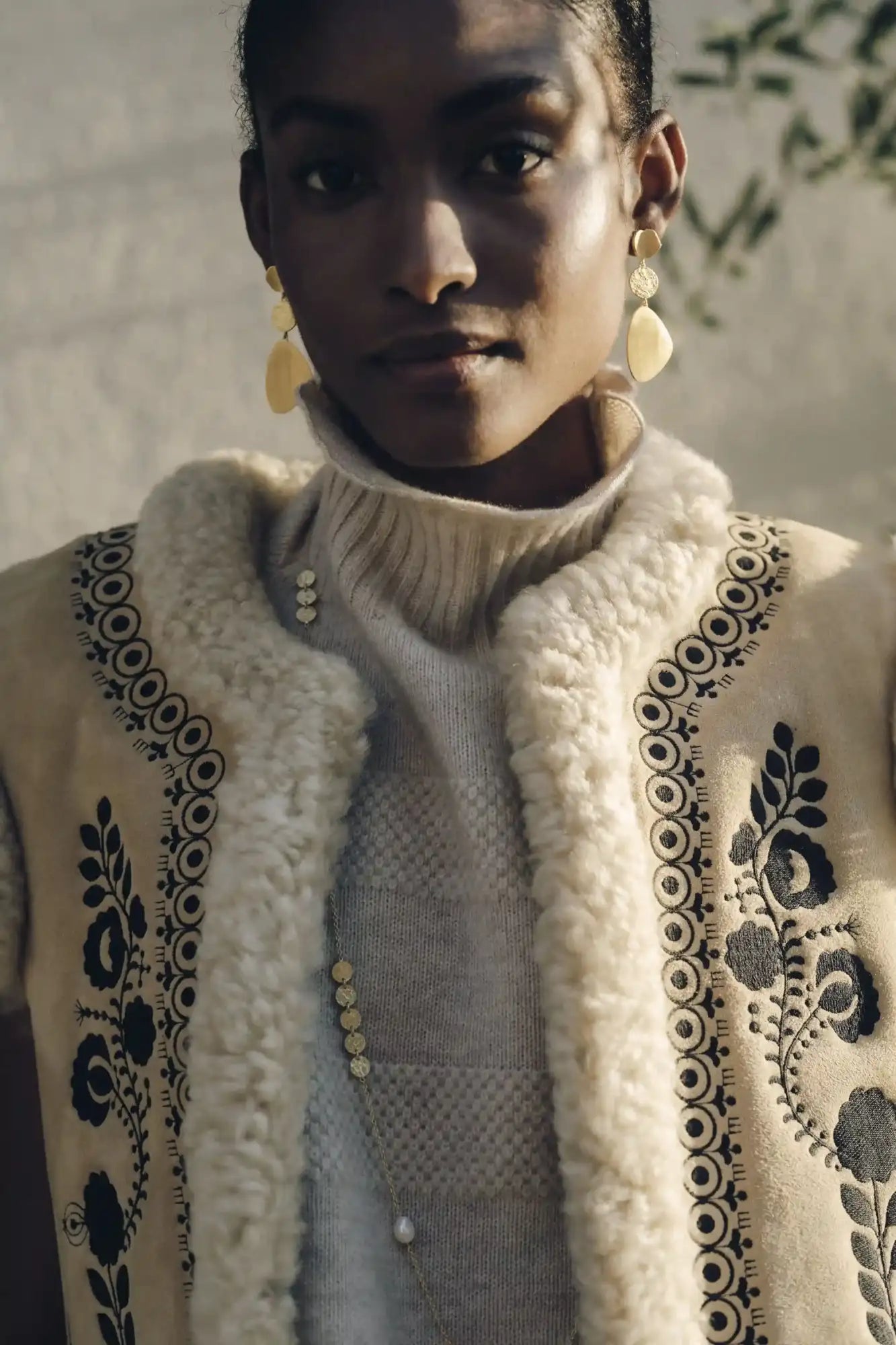 Cream-colored shearling vest with black embroidered floral and circular patterns.