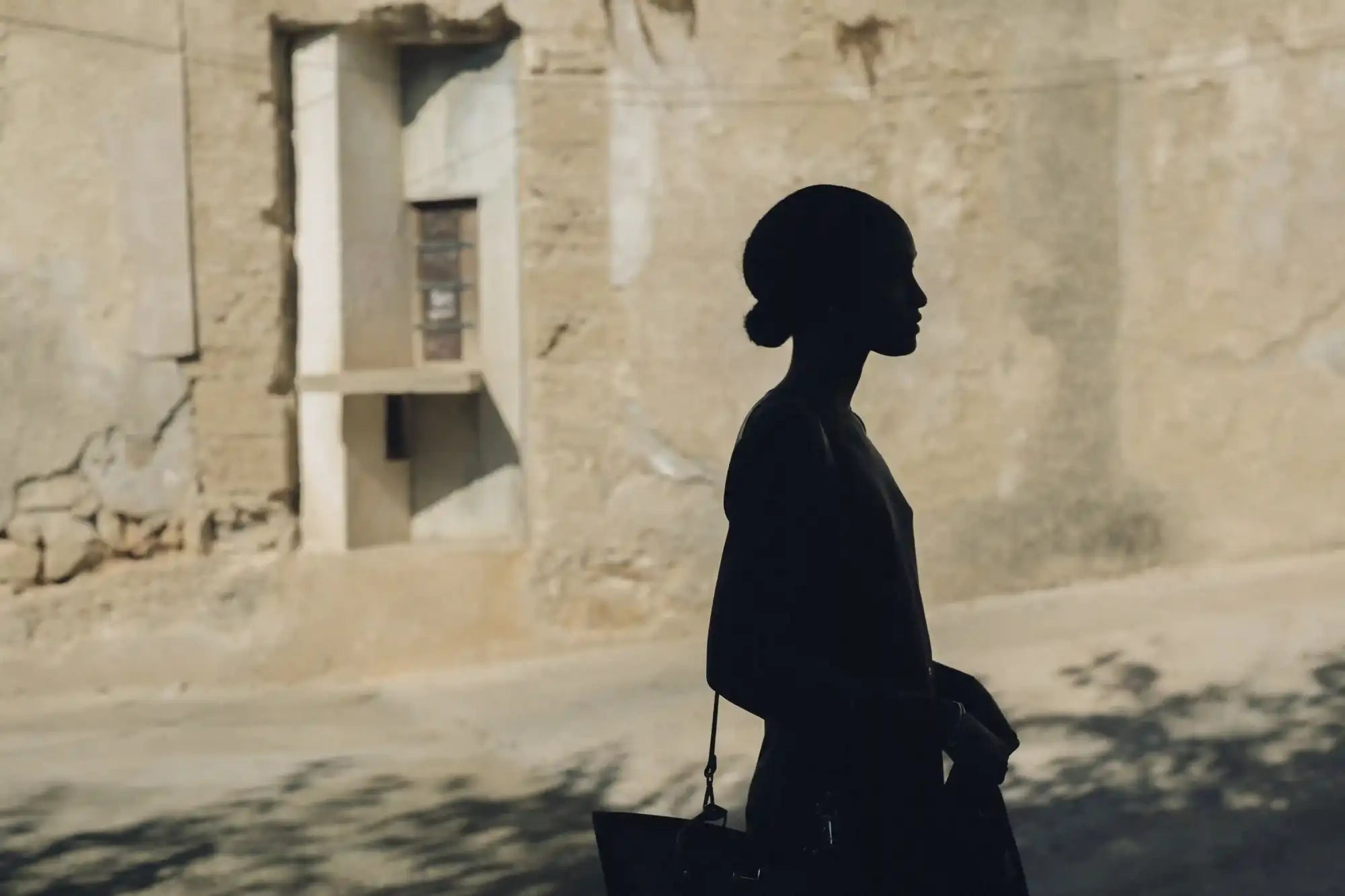 Silhouette of a woman in profile, holding a dark handbag with a thin strap.