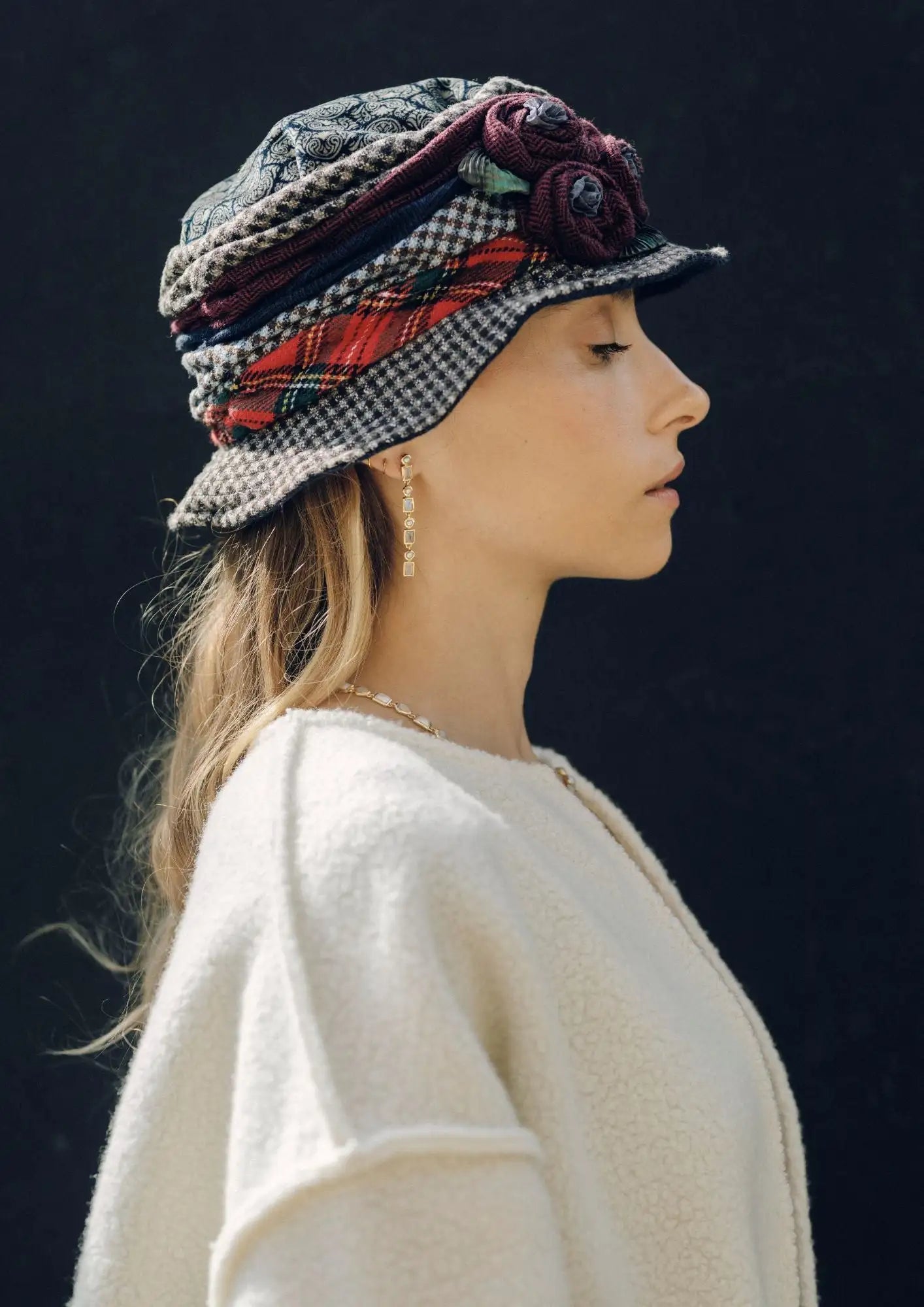 A stylish, patchwork cloche hat featuring a houndstooth pattern in black and white with accents of red plaid fabric and deep burgundy floral embellishments.
