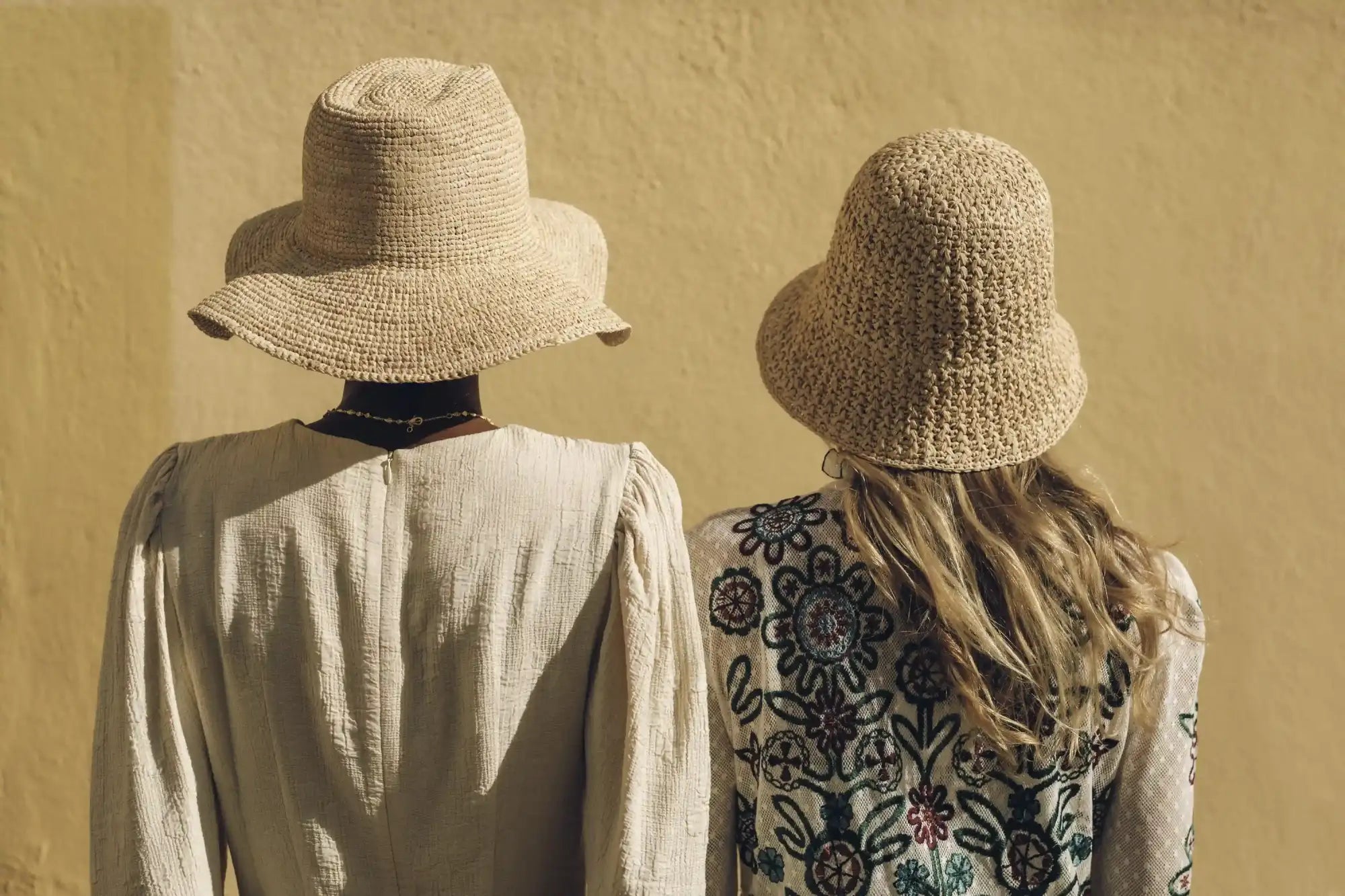 Two women wearing woven straw hats, one with a wide brim and the other with a narrower crown.