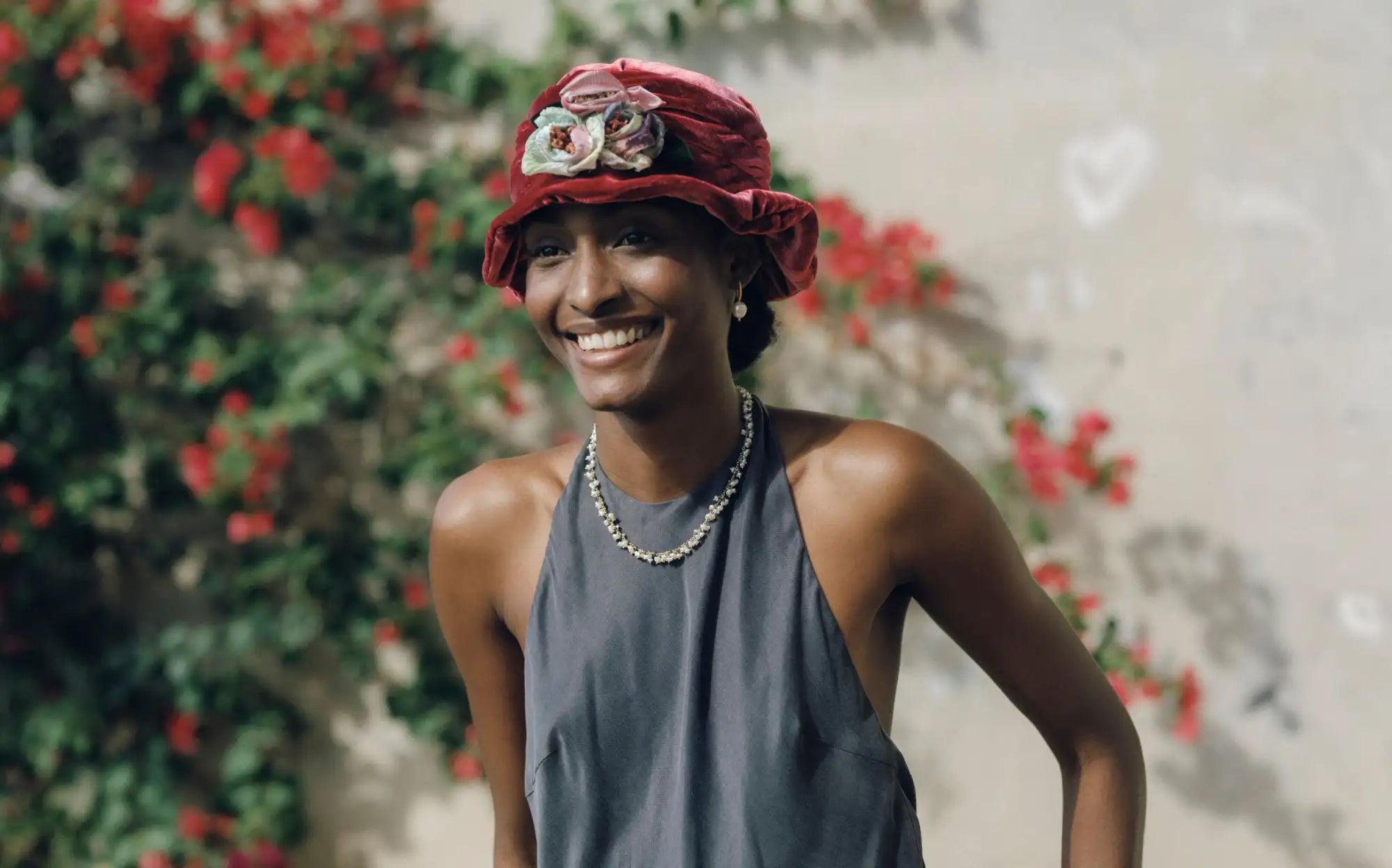 A vibrant red velvet cloche hat adorned with a delicate floral embellishment.